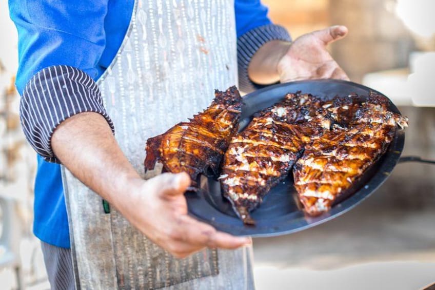 A person holding a pan with grilled meat. 4
