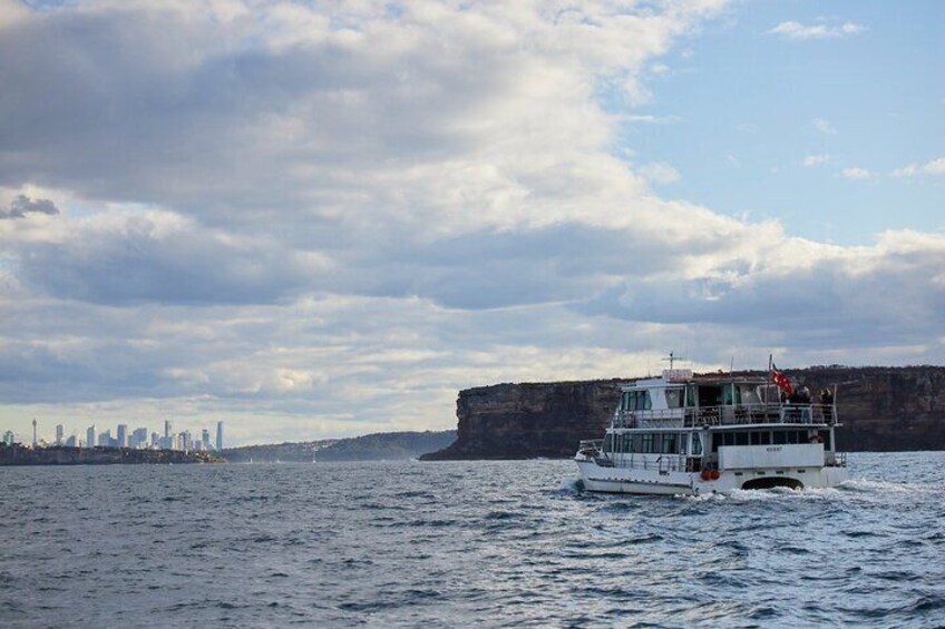 Un bateau sur une étendue d’eau, avec une vue sur les gratte-ciel d’une ville et des falaises en arrière-plan. 2
