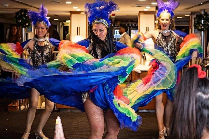 A group of people in colorful costumes with feathered headpieces, holding a rainbow-colored fabric. 2