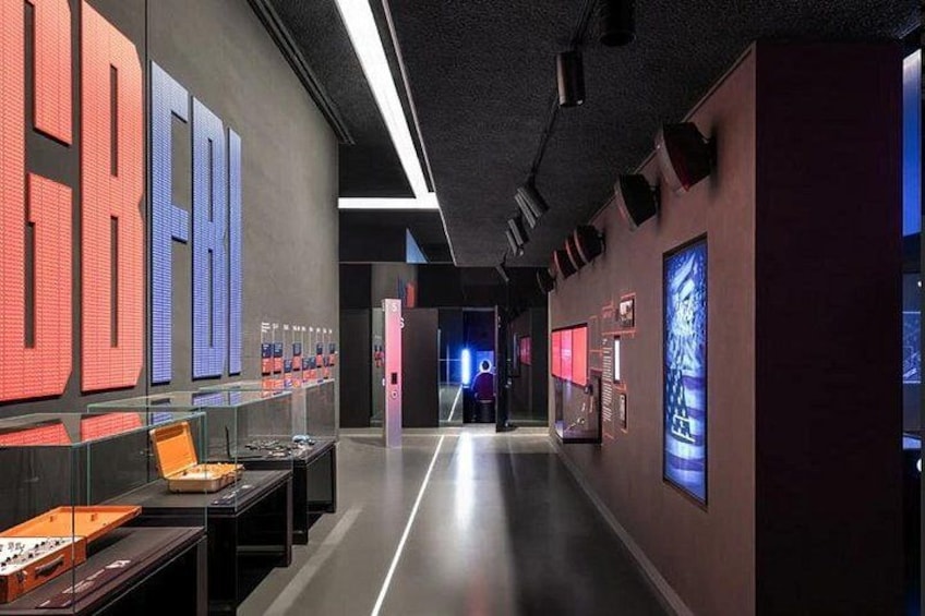 Ein moderner Ausstellungsraum mit großen digitalen Bildschirmen, Glasvitrinen und einem zentralen Gang. 5