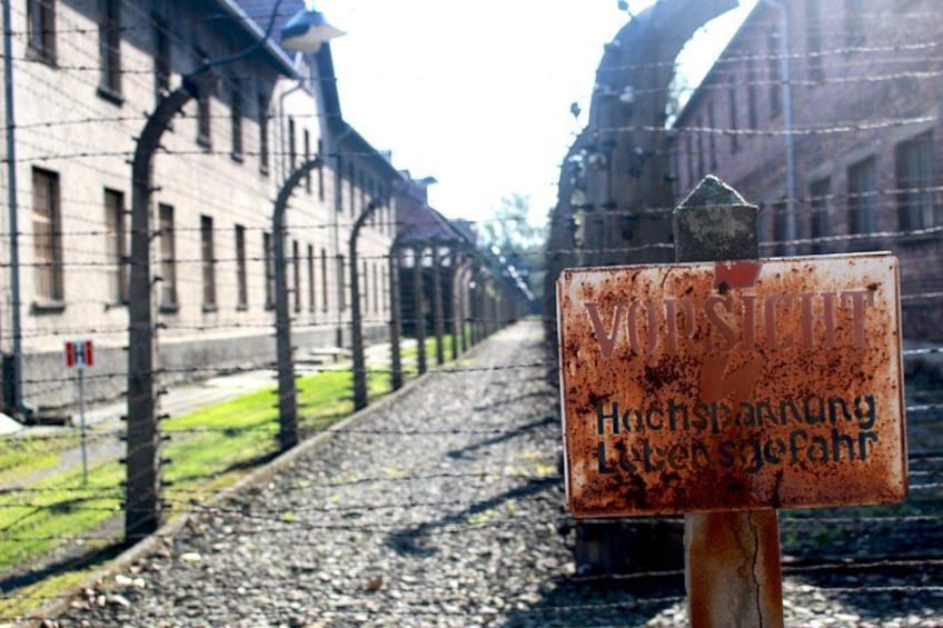 Ein verrostetes Schild mit deutschem Text vor einem Gebäude mit Stacheldraht. 3