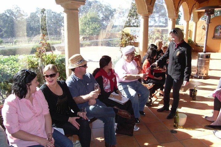 A group of people seated outdoors under a covered area with a view of a garden. 2