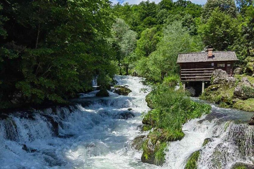A river flowing through a forest with a wooden cabin on a bridge. 1