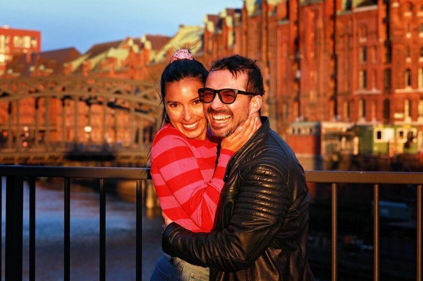 A couple embracing on a bridge with a river and buildings in the background. 3