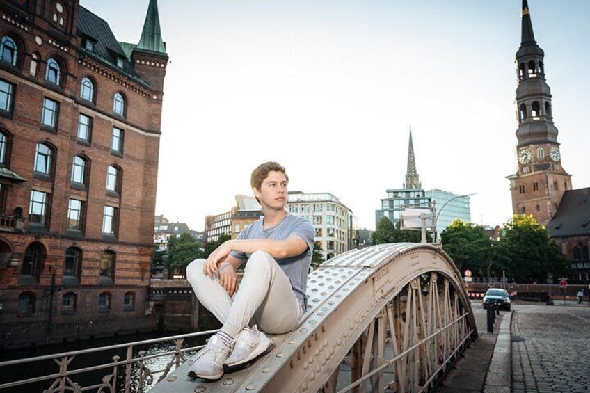 Eine Person sitzt auf einer Brücke, im Hintergrund historische Gebäude und ein Kirchturm. 3