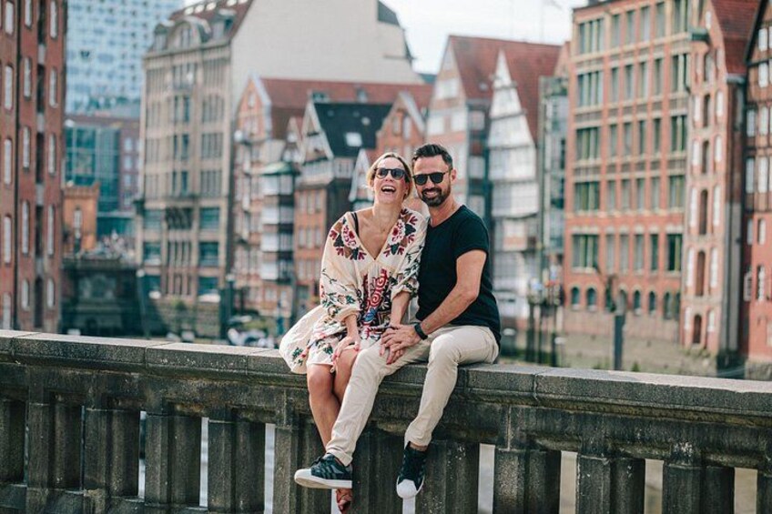 A couple sitting on a bridge with a cityscape in the background. 2