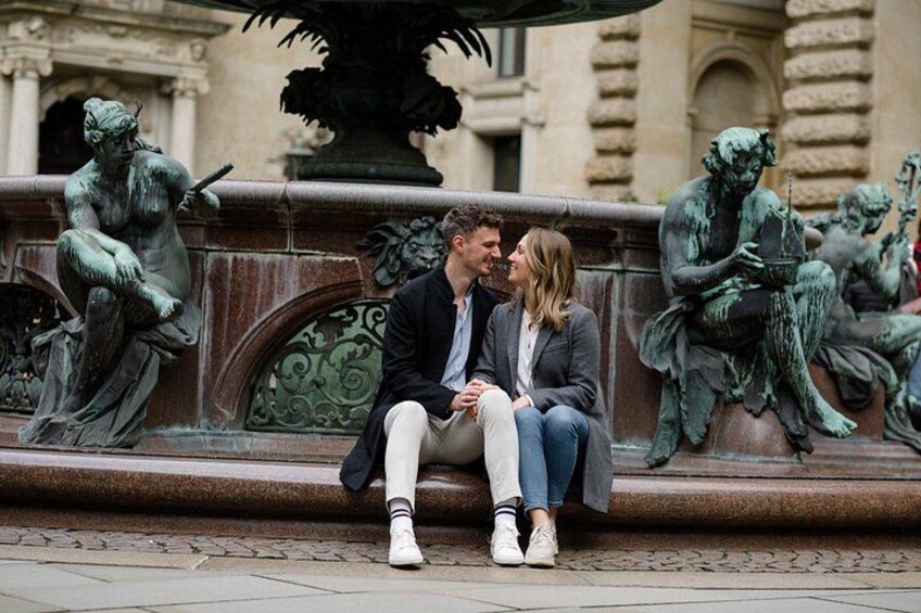 A couple sitting on a bench in front of a fountain with bronze statues. 5