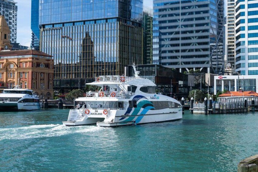 A white yacht with blue accents named 'Fool's Gold' in a harbor with modern buildings in the background. 3
