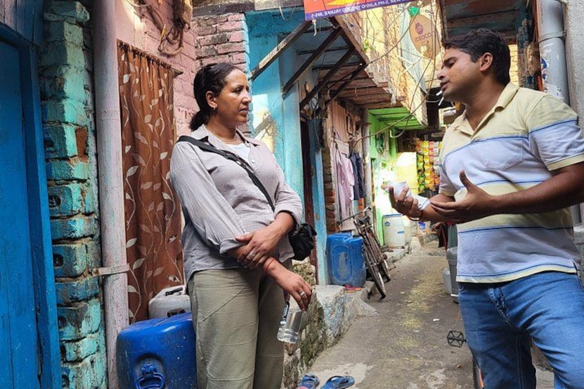 Two people conversing in a narrow alleyway with brick walls and a blue water container. 5