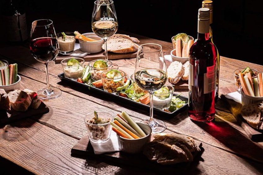 A wooden table with various food items, glasses of wine, and a bottle of red wine. 5