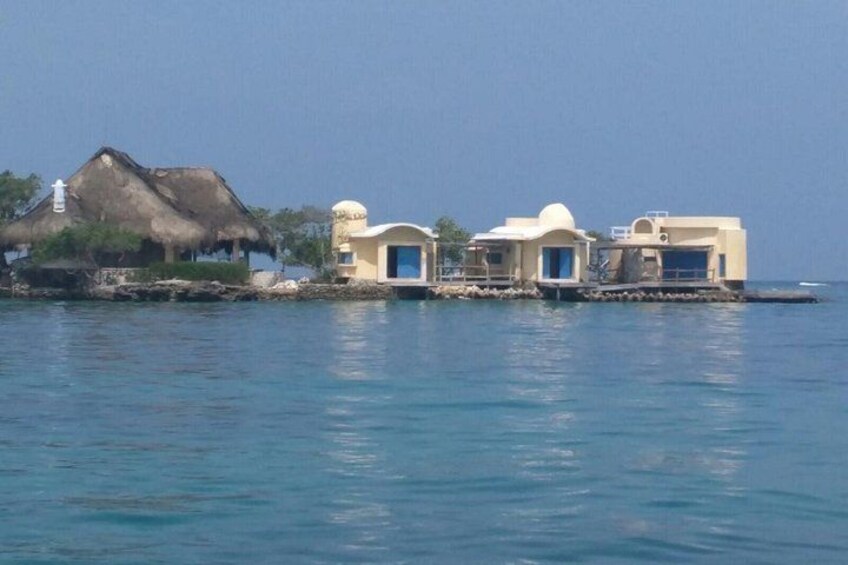 A coastal scene with a thatched-roof house and several modern buildings on stilts over the water. 5