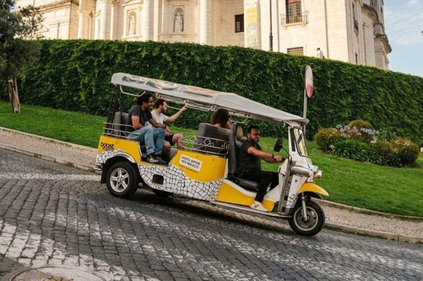 A yellow and white vintage car with passengers, parked on a cobblestone street. 1