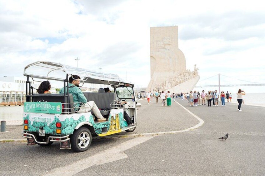 A colorful three-wheeled vehicle parked on a paved area with a large stone monument in the background. 4