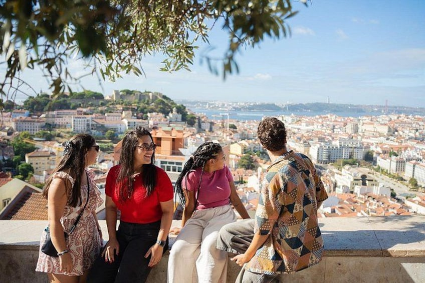 A group of people sitting on a ledge overlooking a cityscape with buildings and hills. 2