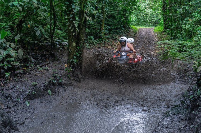 Una persona guida un quad attraverso un sentiero fangoso, circondato da una fitta foresta. 5