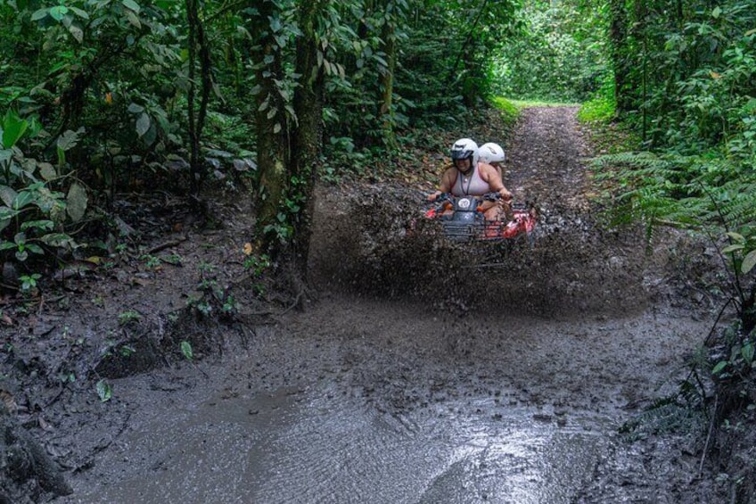 Iemand rijdt op een quad door een modderige route, omringd door dicht bos. 5