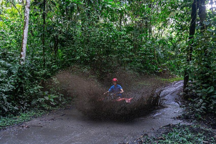 A person riding a motorcycle through a muddy path surrounded by dense forest. 4