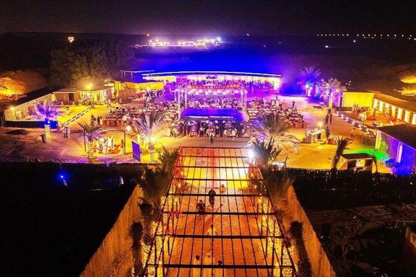 A brightly lit outdoor event area with a stage and seating arrangements. 2
