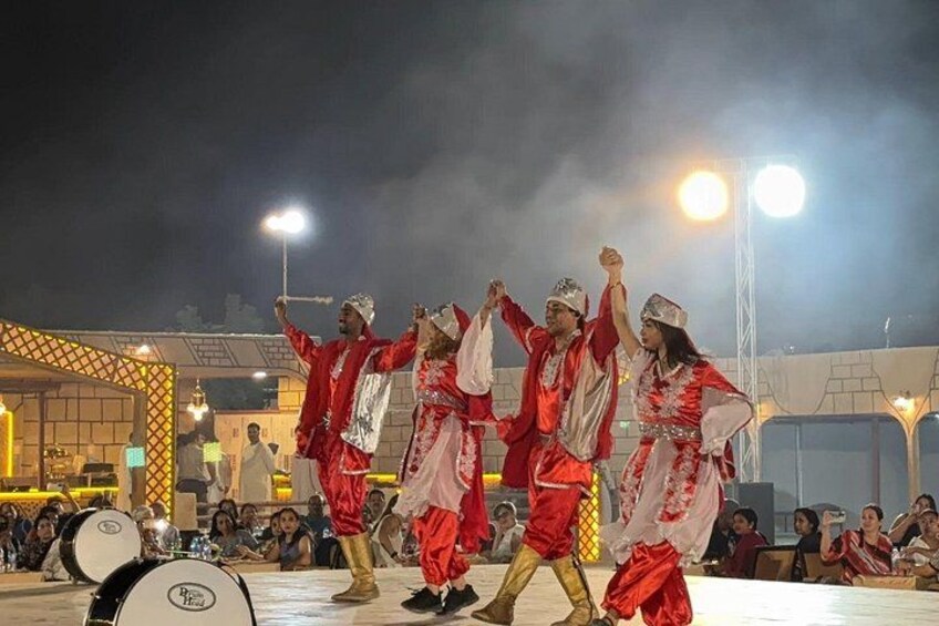 A group performing a traditional dance on a stage with a crowd watching. 4