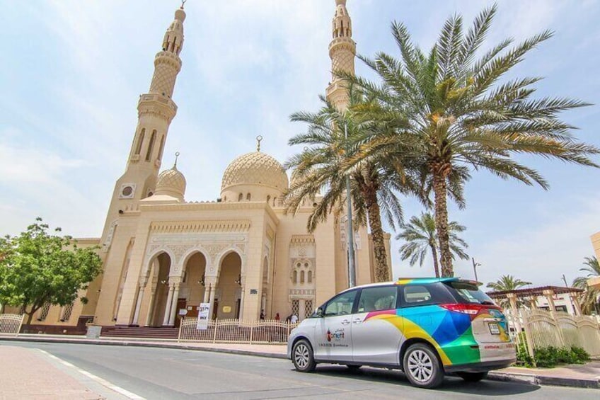 A mosque with two minarets and domes, palm trees, and a parked car. 5