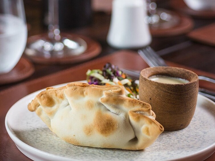 A plate with a pastry and a small cup of sauce. 4