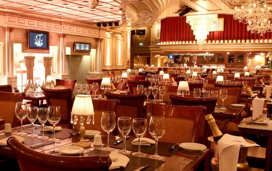 A luxurious dining room with ornate chandeliers, red curtains, and elegantly set tables with wine glasses and cutlery. 2