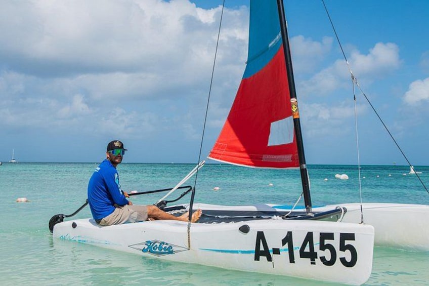 A person sailing a catamaran with a red and blue sail, on clear turquoise water. 3