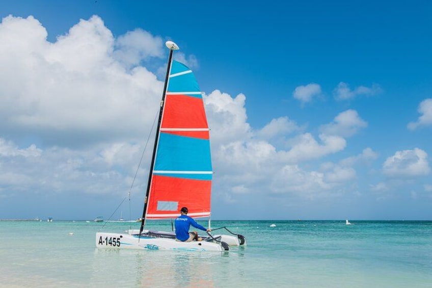 A sailboat with a colorful sail on calm turquoise water under a clear sky. 1