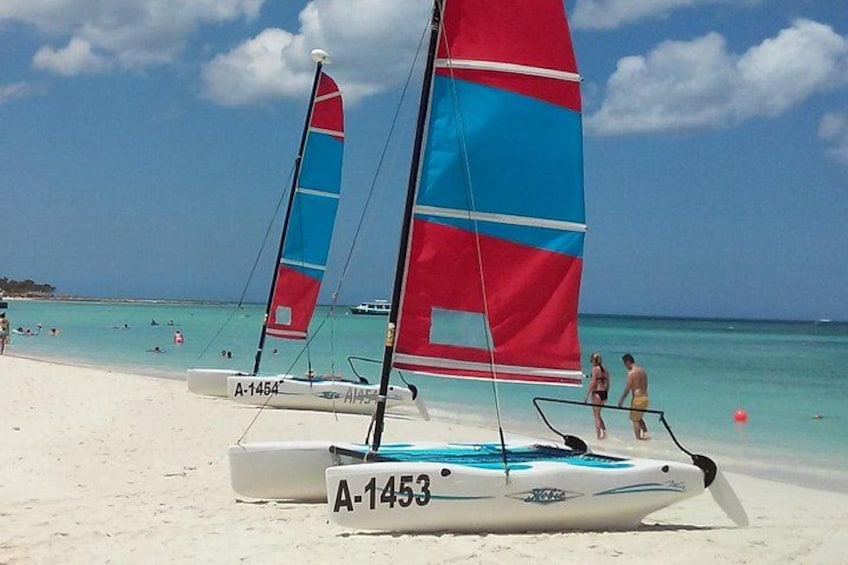 Sailboats on a beach with clear turquoise water and a few people in the distance. 4