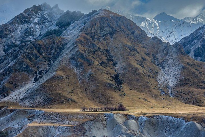 Een bergachtig landschap met besneeuwde toppen, een vallei met schaarse begroeiing en een heldere lucht. 5