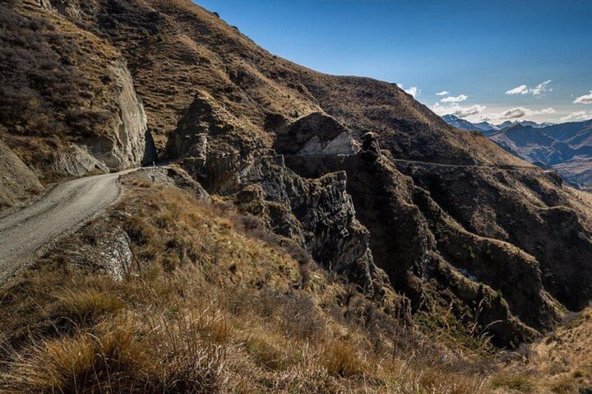 Een kronkelende bergweg, rotsachtig terrein en verre bergen onder een heldere lucht. 3