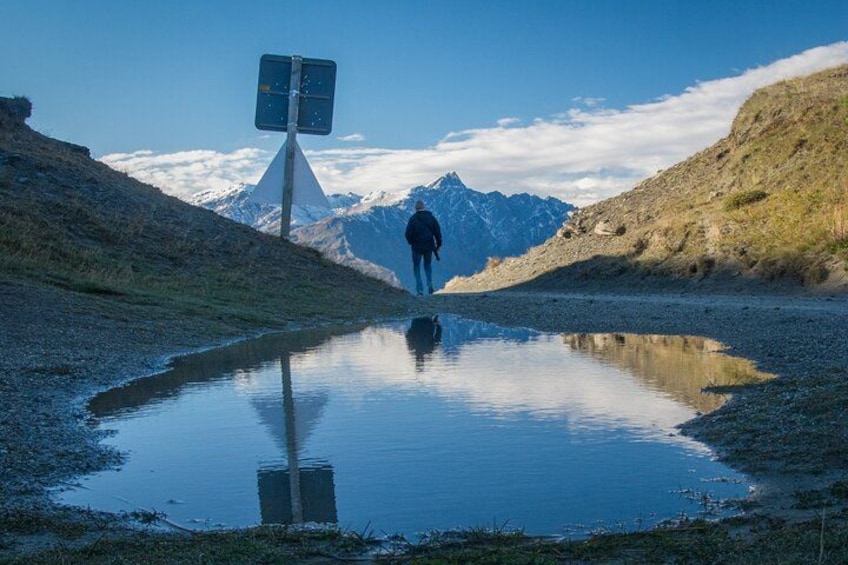 Een persoon loopt op een bergketen af, met een richtingwijzer in een spiegelglad plaswater. 2