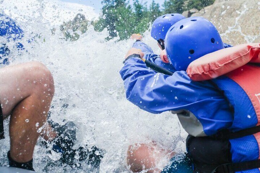 A person in a blue jacket and helmet, wearing a red life jacket, paddling a kayak. 2