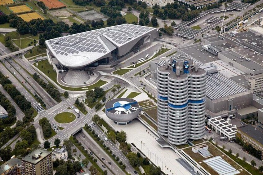 An urban area with a modern building, a circular structure with a logo, and a tall cylindrical building. 3