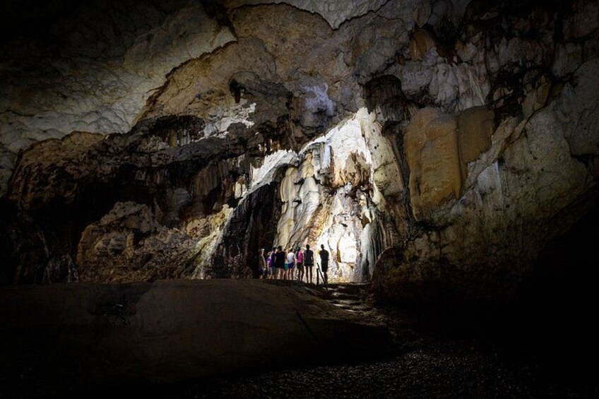 A cave with stalactites and stalagmites, a group of people standing at the entrance, and a large rock formation in the foreground. 3