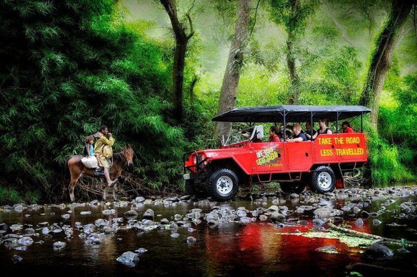 A red vehicle with passengers and a horse crossing a river. 1