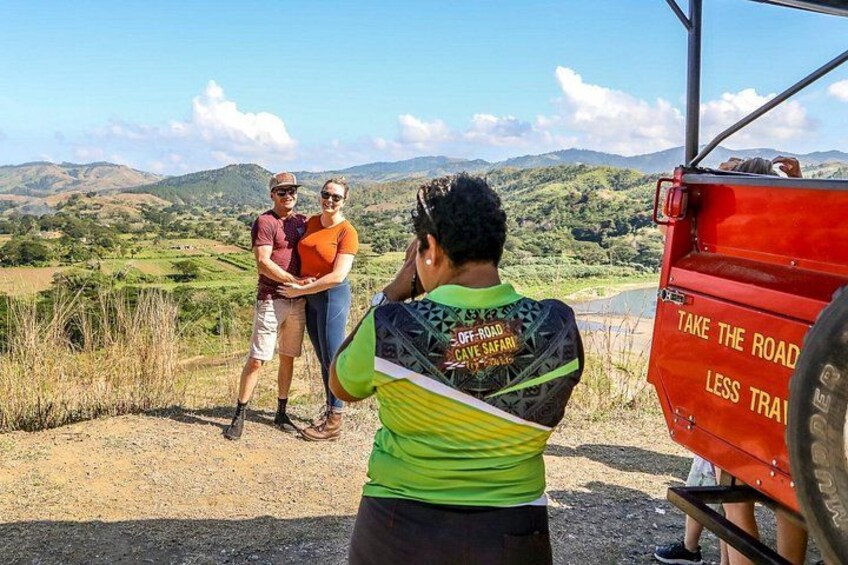 A person taking a photo of three people standing on a dirt road with a scenic view of hills in the background. 2
