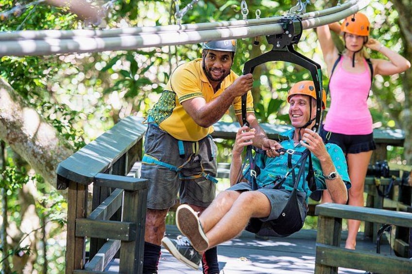A person being assisted on a zip line, surrounded by trees and wooden structures. 1