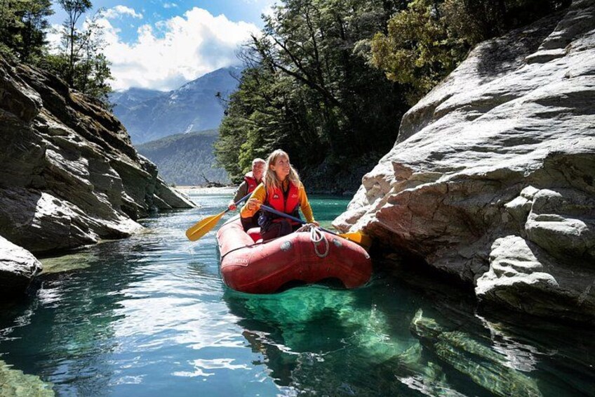 Eine Person in einer roten Floß auf einem schmalen Fluss, umgeben von felsigem Gelände und Bäumen. 3