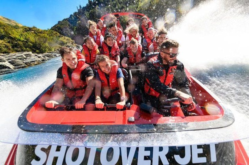 Eine Gruppe von Menschen in einem roten Jetski mit der Aufschrift 'SHOTOVERJET', die einen Fluss befährt. 4
