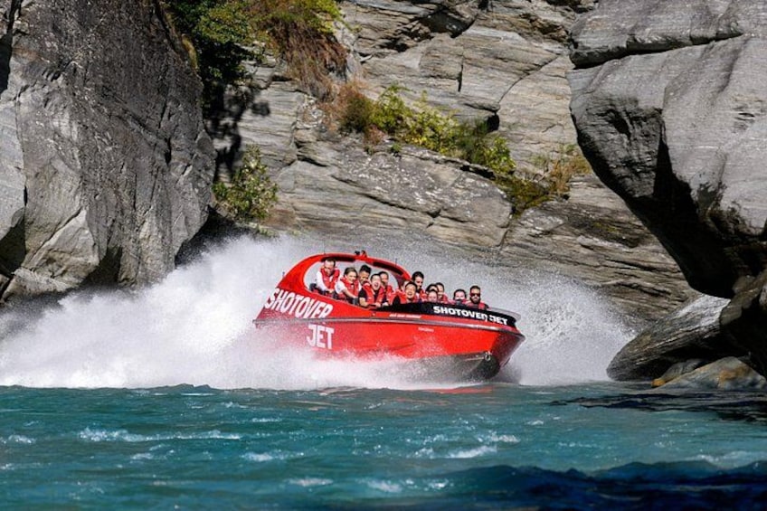 En röd snabbåt med texten ”SHOTOVERJET” på skrovet, som färdas på vattnet nära klippiga branter. 4