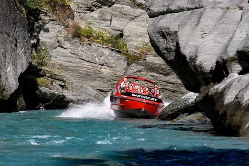 A red boat with passengers navigating through a rocky waterway. 5