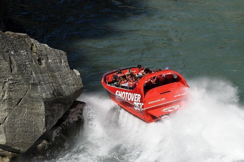 A red speedboat with 'SHOTOVER 35' written on it, speeding through water near a large rock formation. 3