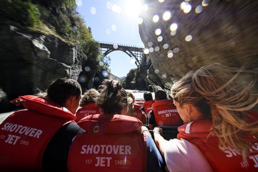 En grupp personer i röda västar med texten ”SHOTOVER”, som går längs en väg med en bro i bakgrunden. 3