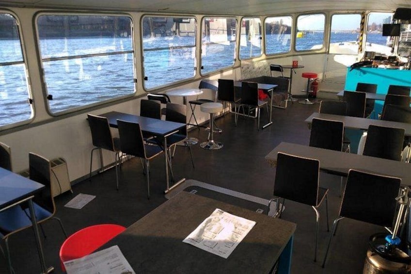 A dining area on a boat with tables and chairs, large windows, and a view of the water. 3