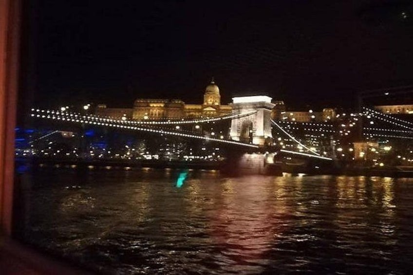 A lit bridge at night with reflections on water, a domed building, and string lights. 2