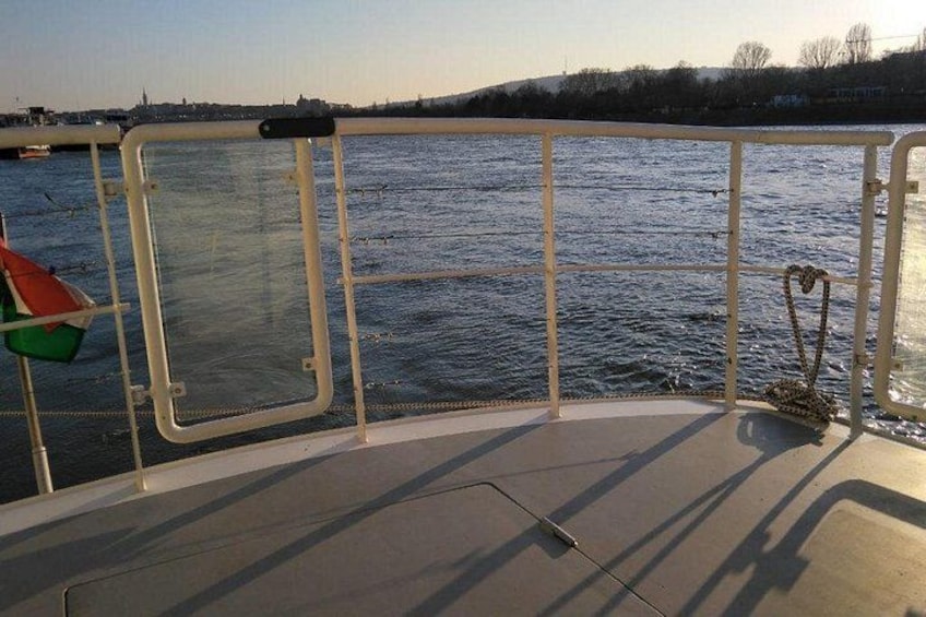 A boat deck with a metal railing, a rope, and a view of a river. 4