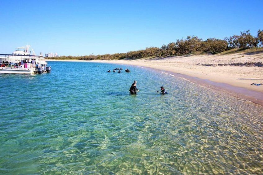A beach with clear shallow waters, a boat, and people swimming. 1
