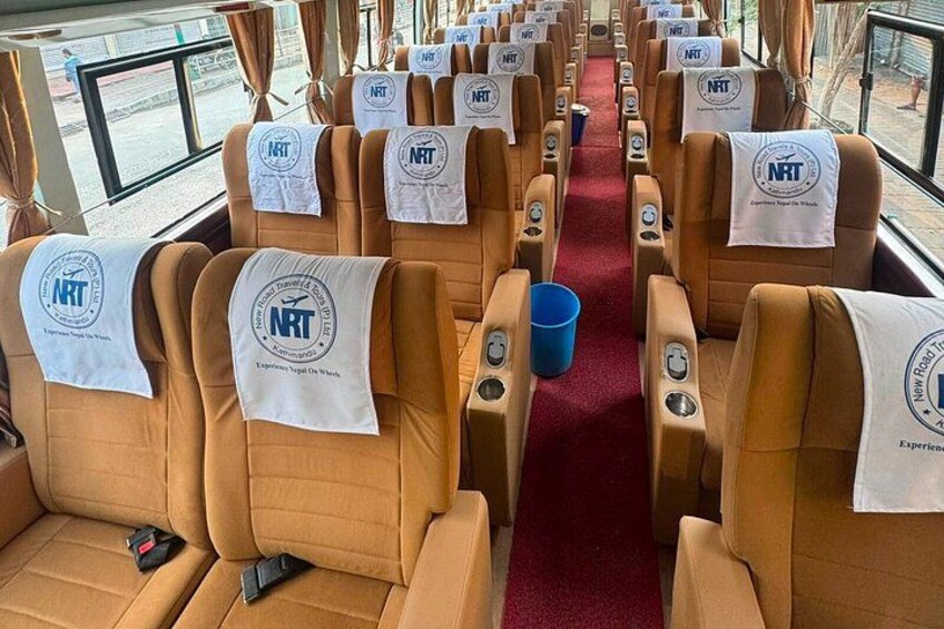 A train carriage with rows of seats, each with a white cloth displaying the NRT logo. 1