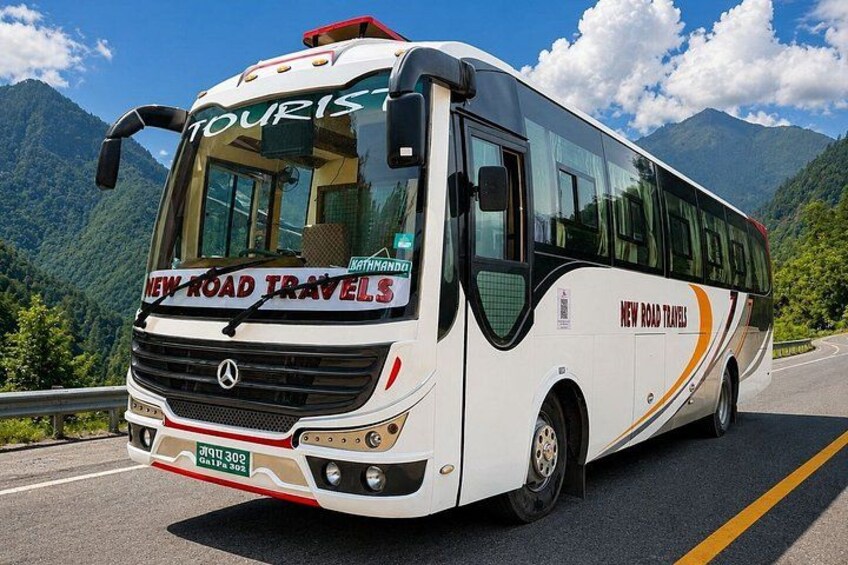 A white bus with 'NEW ROAD TRAVELS' written on the side, driving on a road with mountains in the background. 2